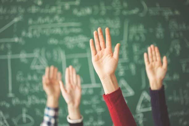 Aspiring students displaying enthusiasm by raising their hands in front of a blackboard, exemplifying the importance of student admissions and parent involvement in schools.
