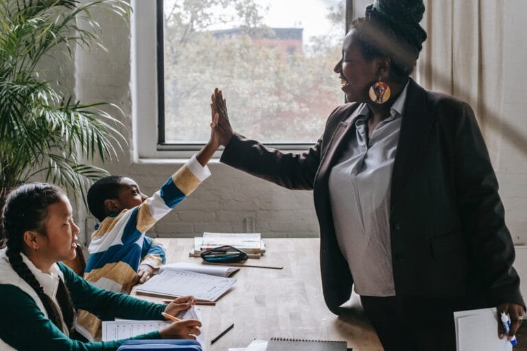 A woman giving a high five to a group of children at a desk during student admissions registration form.