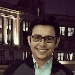 A man in glasses smiling in front of a building at night.