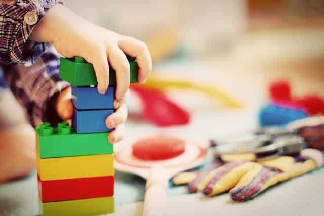 A child in kindergarten is playing with a stack of colorful lego blocks.