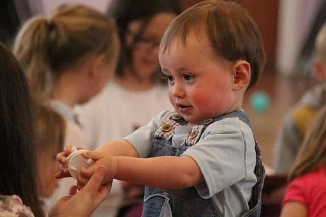 A baby is playing with a toy in front of a group of people as part of the kindergarten marketing campaign.